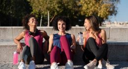 Three women sitting on outdoor steps, each holding a water bottle, engaged in conversation